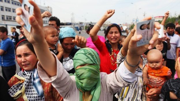 نساء من الإيغور يرفعن هويات المعتقلين في مسيرة احتجاجية